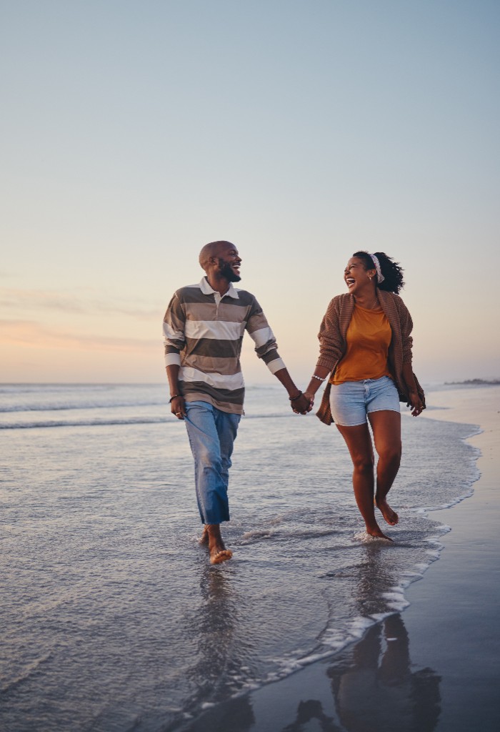 Couple souriant se promenant main dans la main sur une plage au coucher du soleil